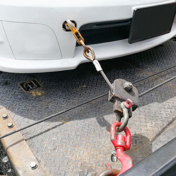 Broken down auto vehicle car towed onto flatbed tow truck with hook and chain